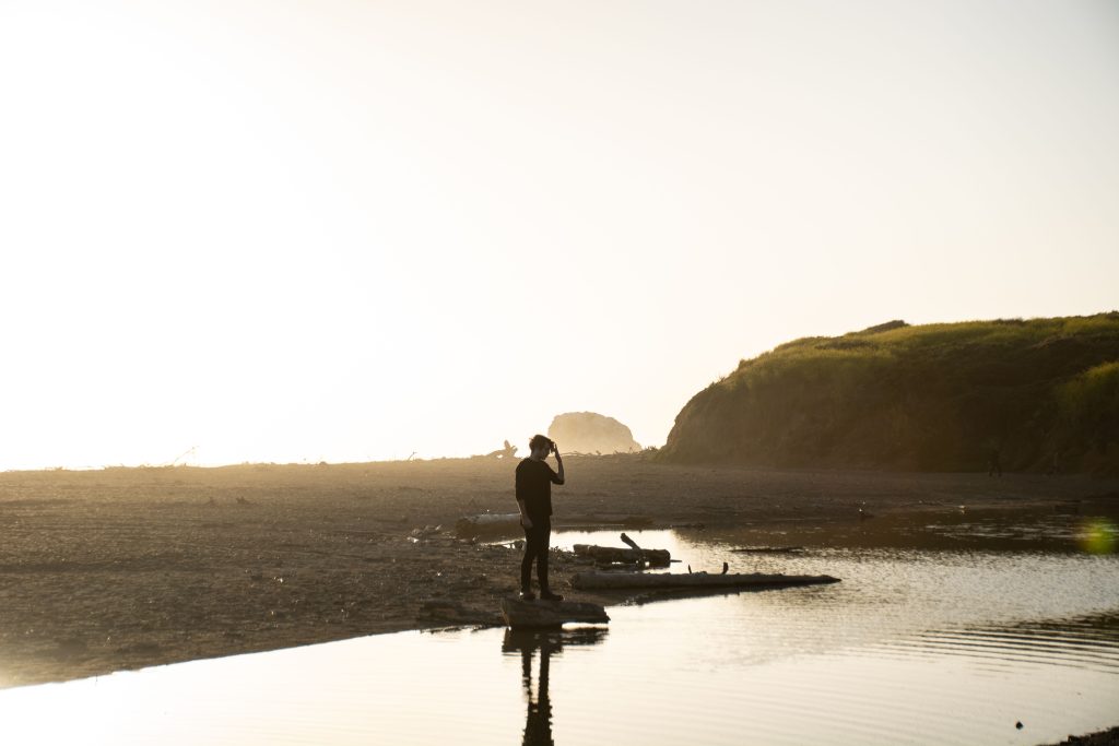 Silhouette of a man in black outfit standing on a coastal shore during sunset, capturing the natural beauty.