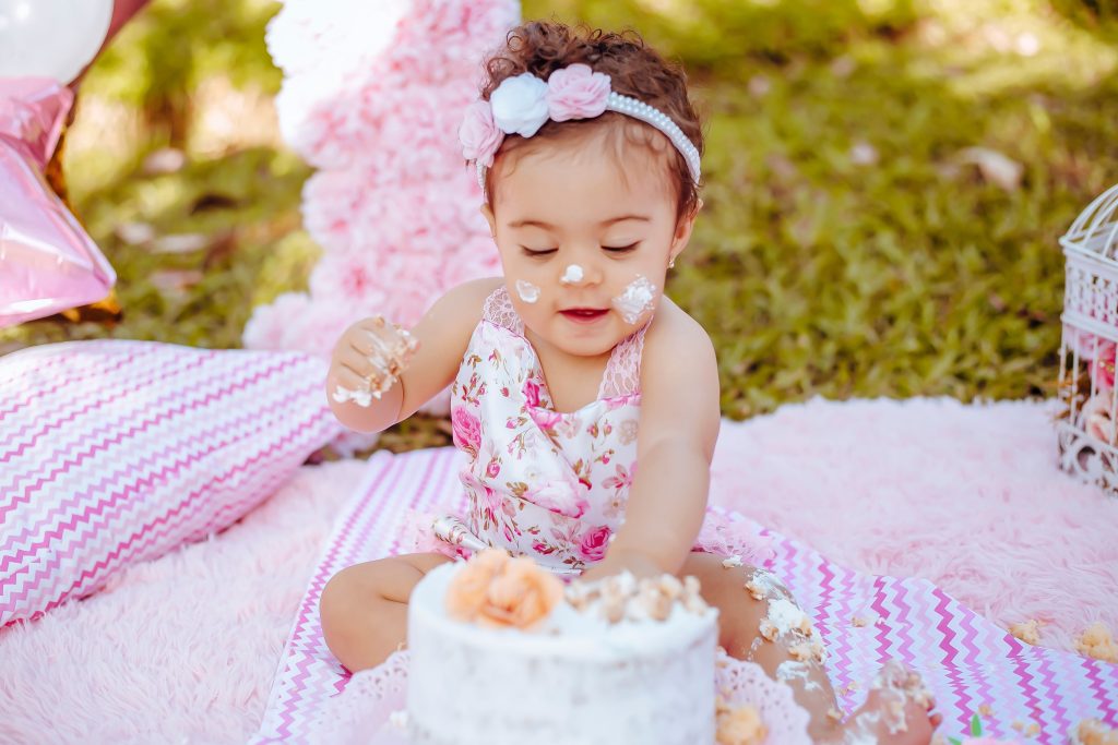 A cute baby with cake on face enjoying an outdoor birthday picnic.