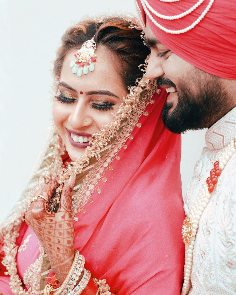 Smiling bride and groom in vibrant traditional Indian attire share a joyful moment.