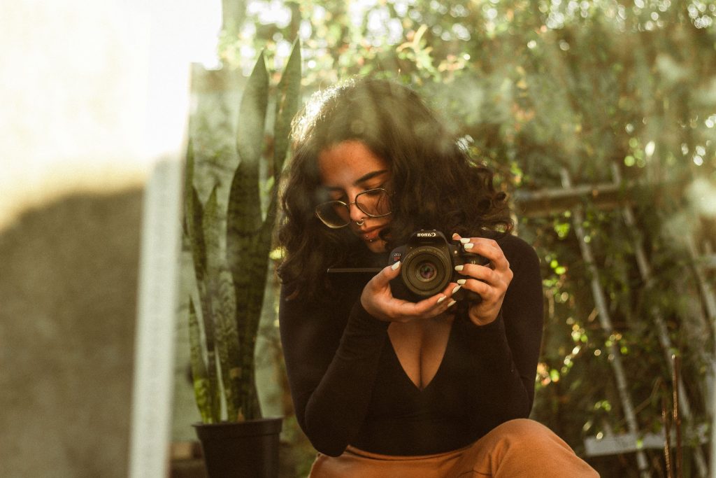 A woman takes a mirror selfie holding a camera, surrounded by greenery.